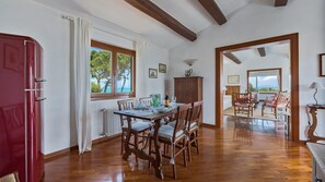 Zona pranzo con tavolo in legno apparecchiato per quattro persone, un armadietto rosso e vista mare attraverso ampie finestre.