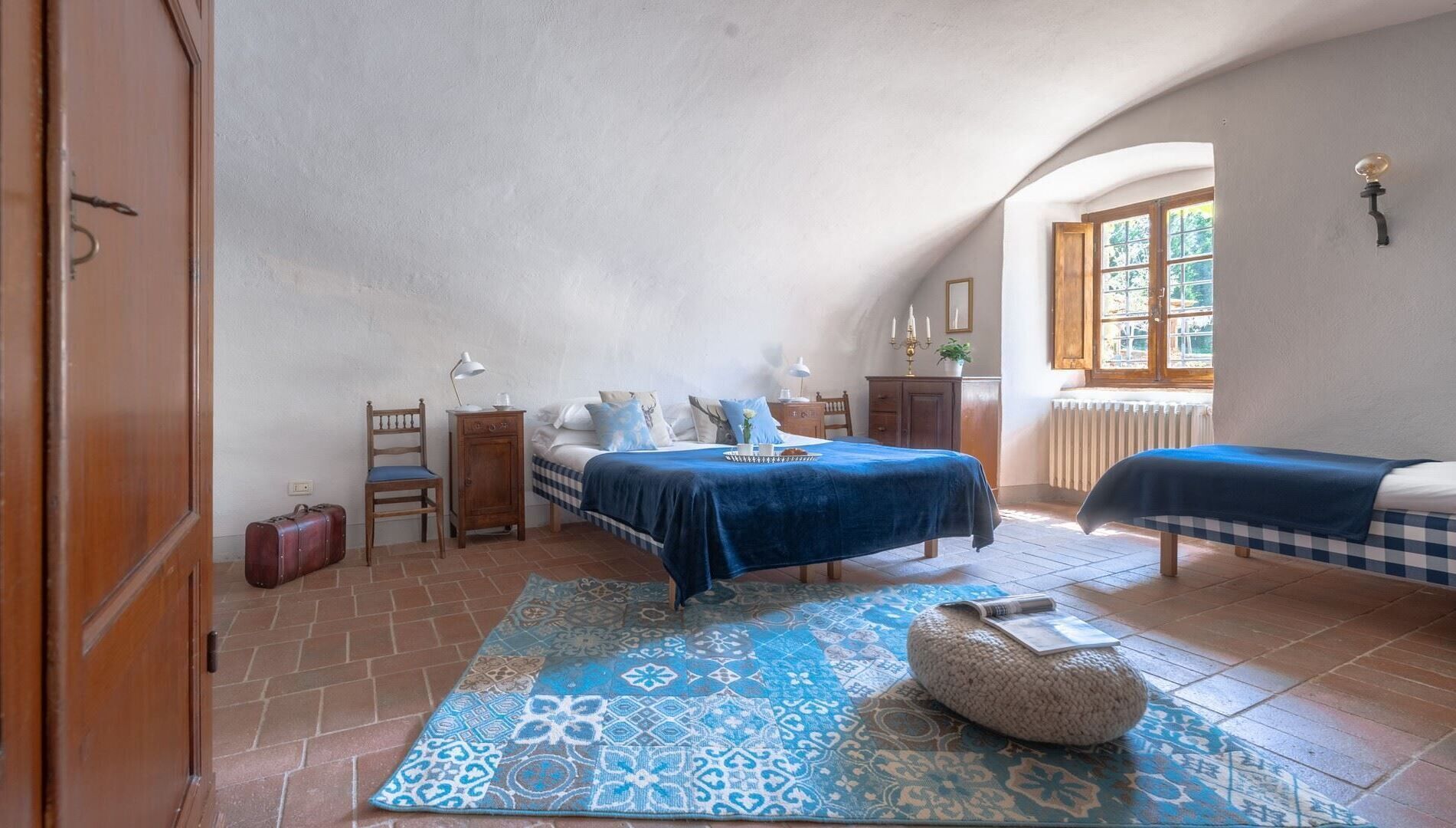 Ein Schlafzimmer mit zwei Betten, einem großen Fenster, einer Heizung und einem gemusterten Teppich.