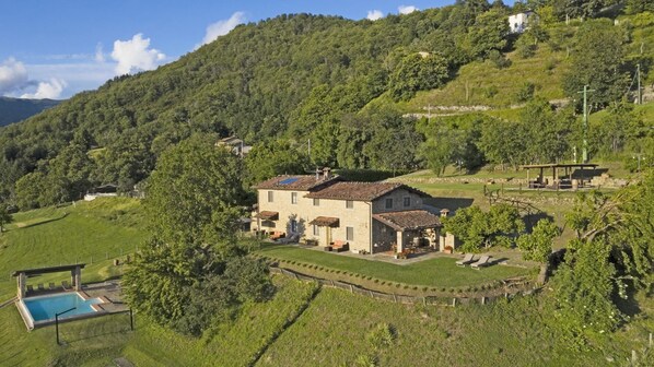 Une maison avec une piscine, entourée d’une végétation luxuriante et de collines.