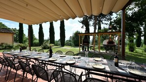 Un área de comedor al aire libre con mesa y sillas cubiertas, un horno de pizza y una estructura de pérgola.
