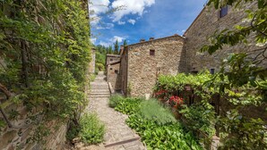 A narrow stone pathway flanked by rustic stone buildings with overgrown vegetation and a clear blue sky. - Il Portico, Montefienali, Gaiole in Chianti, Siena and Chianti (Gaiole in Chianti)