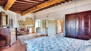Une chambre avec un grand lit, une armoire en bois, un banc et un mur en pierre.