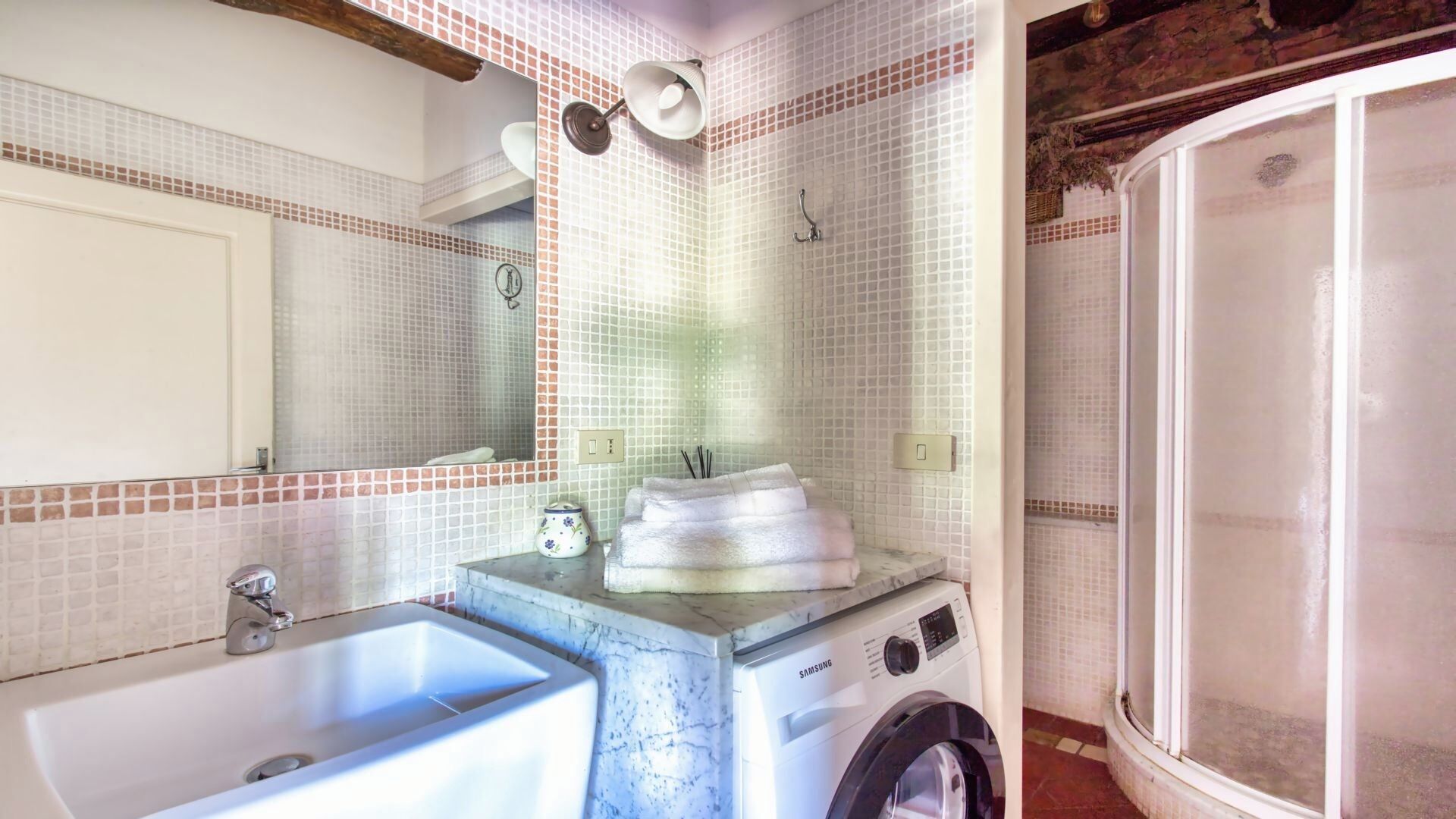 Une salle de bain équipée d’un lavabo, d’un lave-linge, d’un miroir et d’un espace douche.