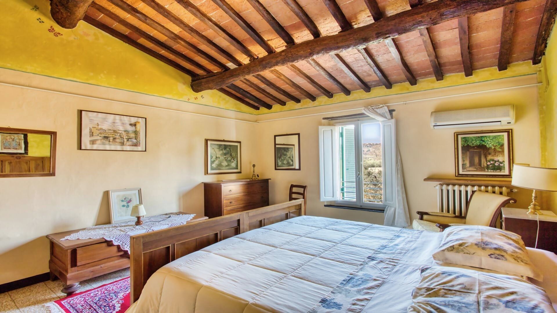 Ein Schlafzimmer mit Holzboden, einem großen Bett, einem Schreibtisch und einem Fenster mit Vorhängen.