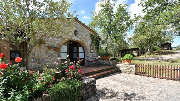 A stone building with a wooden door, a small table with chairs, and a garden with red flowers. - Il Poggetto a Vescinino, Radda in Chianti, Siena and Chianti (Radda in Chianti)