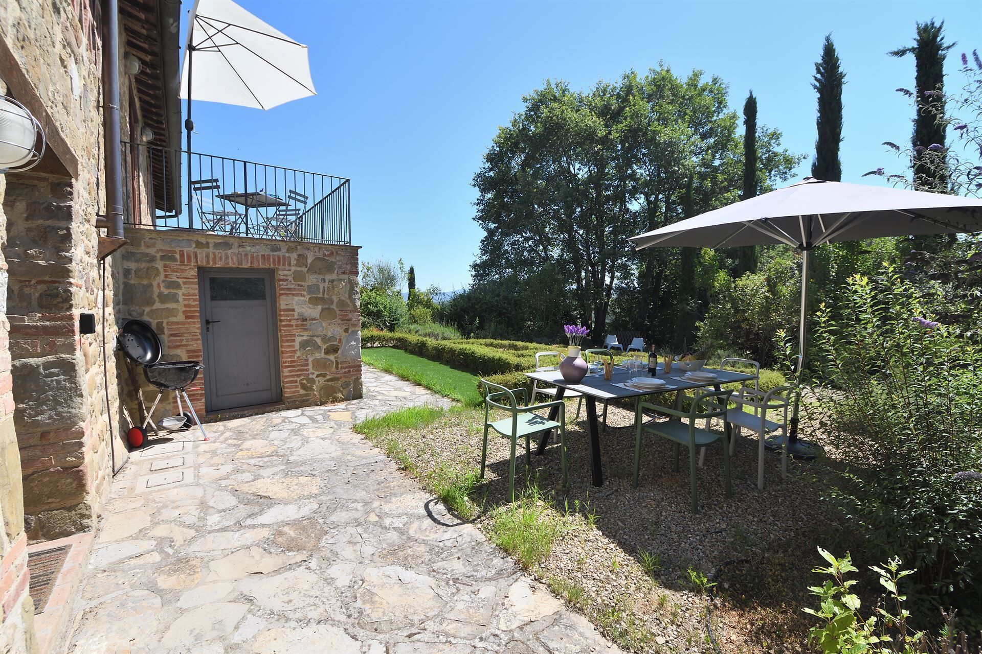 A stone building with a door and a small balcony. There is a table with chairs and an umbrella outside.