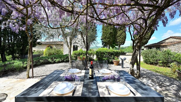 Un espace de restauration en plein air avec une table dressée pour quatre personnes, entouré d’une végétation luxuriante et d’arbres aux fleurs violettes.