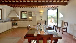 Une cuisine spacieuse avec un coin repas, comprenant une grande table dressée, une vue sur l’extérieur grâce à une porte vitrée et un plafond en bois rustique.