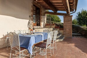 An outdoor patio with a table set for two, surrounded by metal chairs with a blue tablecloth.