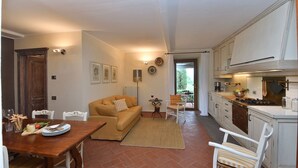 A cozy living room with a sofa, a dining table set with plates and glasses, and a kitchen area with cabinets and a stove. - Athena, Podere di Casalta, Castellina in Chianti, Siena and Chianti (Castellina in Chianti)