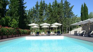 Ein klares Schwimmbecken mit Liegestühlen und Sonnenschirmen, umgeben von Bäumen und einer Steinmauer.