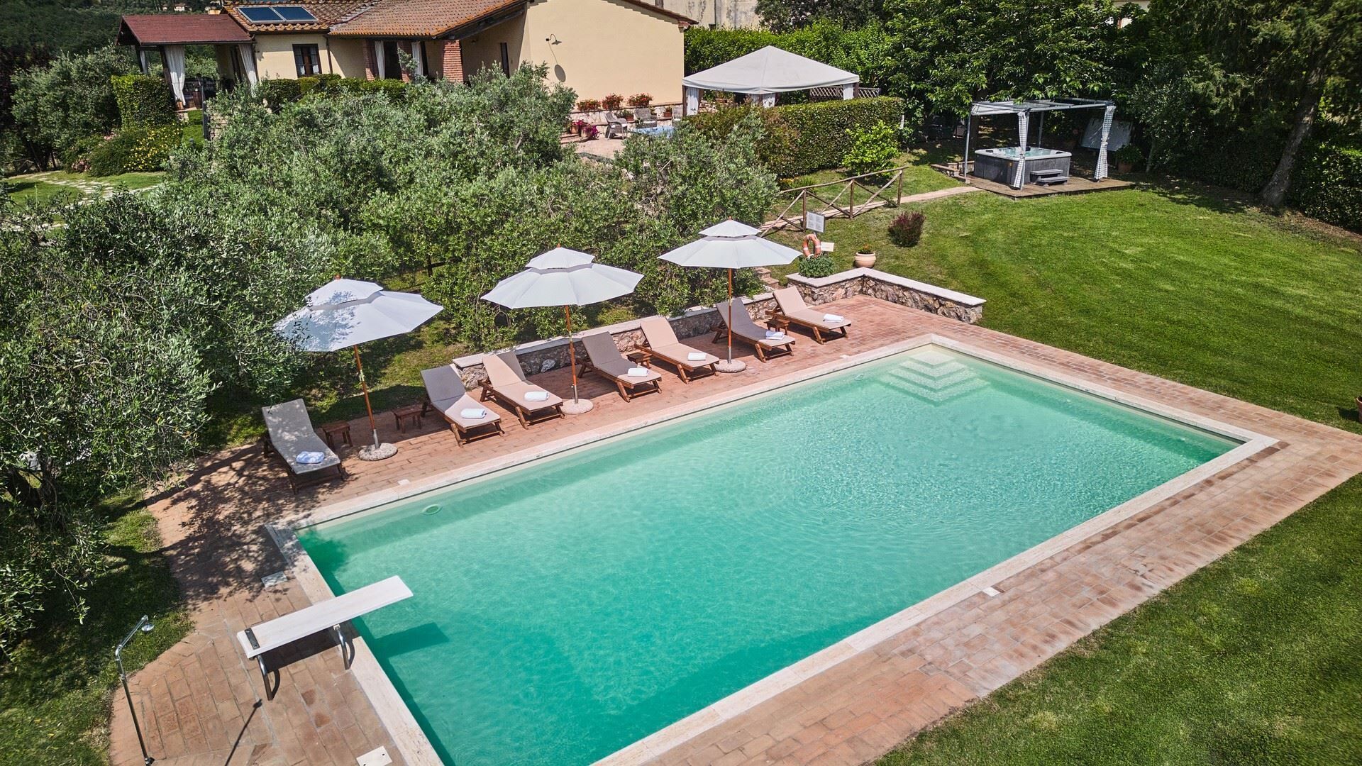 A rectangular swimming pool with a brick border, surrounded by a grassy lawn and trees.