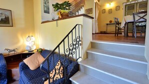 Uma escadaria leva a uma área de refeições com uma mesa e cadeiras, um sofá com almofada e uma planta em vaso no patamar.