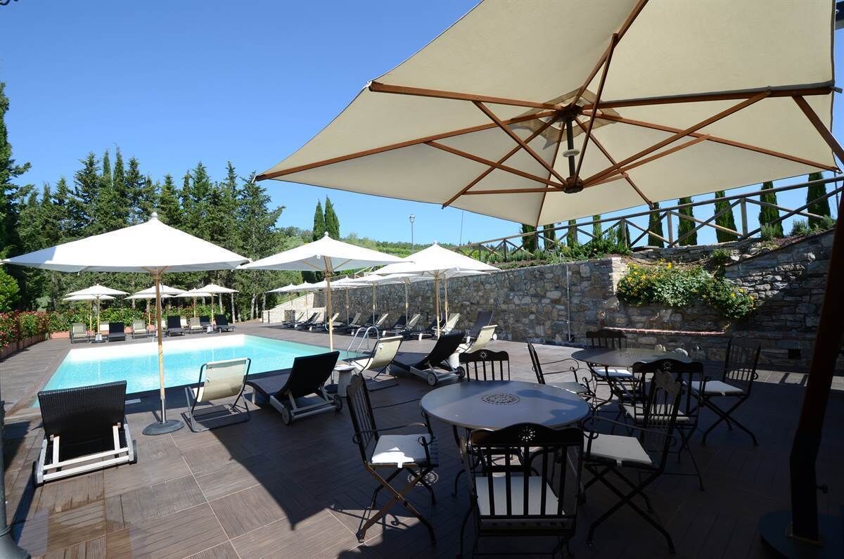 A poolside area with lounge chairs and umbrellas, a stone wall, and a clear blue sky.