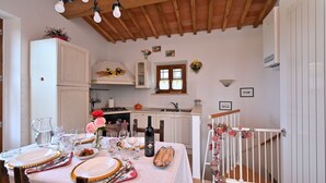 Un coin repas avec une table mise pour le repas, une cuisine en arrière-plan et un escalier avec une rampe.