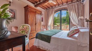 Quarto com cama, cadeira, mesa e janela com cortinas.