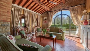 A cozy living room with a stone wall, wooden ceiling beams, and a large arched window.