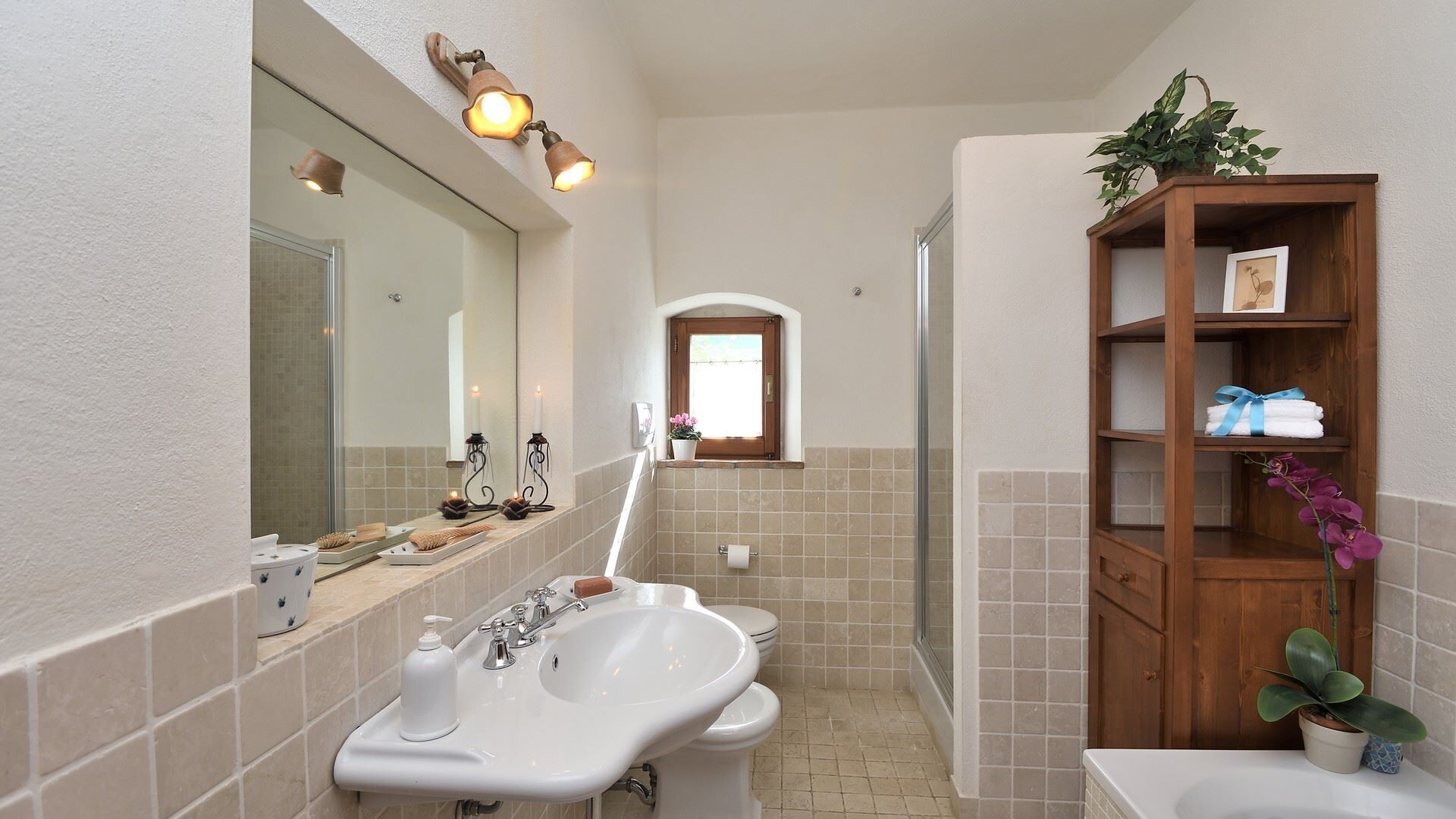 Une salle de bain avec un lavabo, un miroir et une étagère en bois où sont posées des serviettes et une plante.