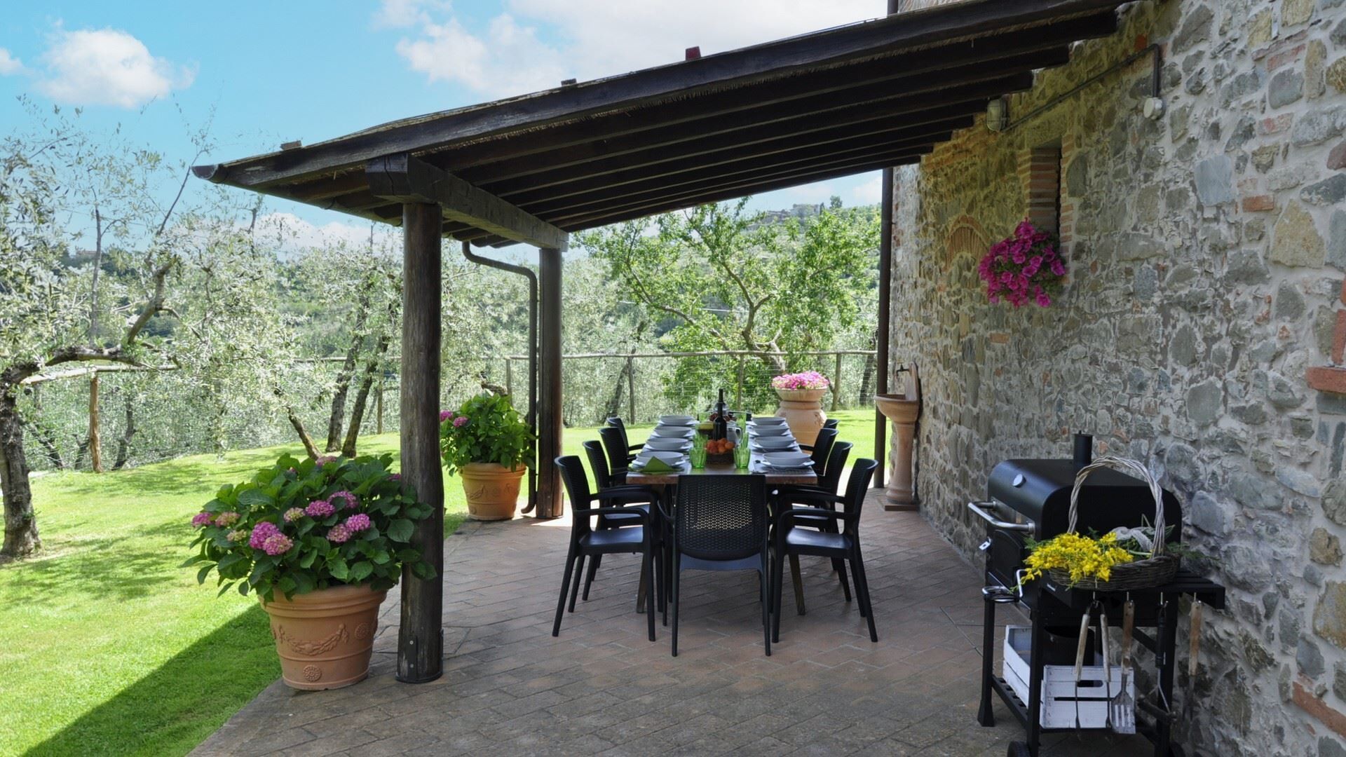 An outdoor patio with a stone wall, a grill, and potted plants.