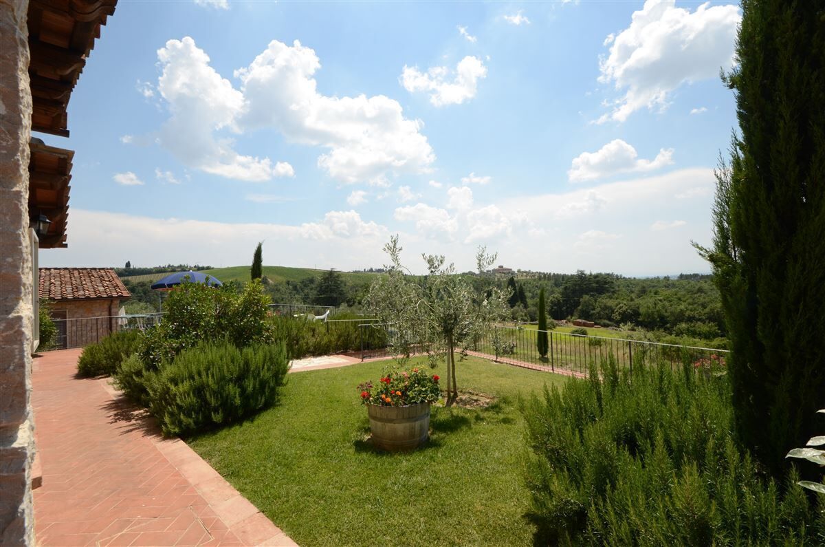 A garden with a paved pathway, a wooden pergola, and a view of the countryside.
