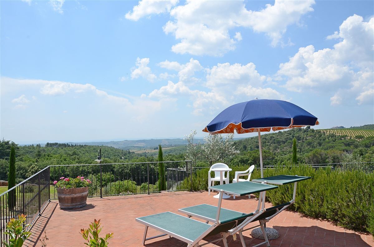 Una terraza con vistas al campo, un paraguas azul y dos sillones de descanso.