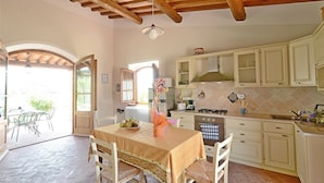 Une cuisine avec des meubles blancs, une table à manger avec des chaises et un sol carrelé.