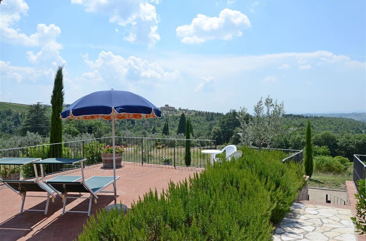 A terrace with outdoor seating, a large umbrella, and a scenic view of the countryside.
