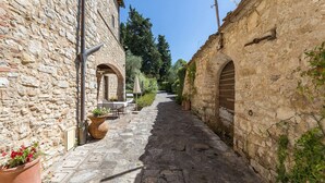 Un étroit sentier pavé, bordé de bâtiments dotés de portes en arc de cercle et d’espaces aménagés pour s’asseoir à l’extérieur.
