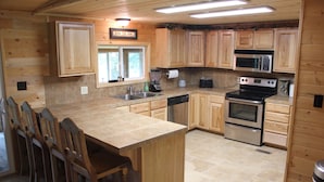 A kitchen with wooden cabinets, a large island with bar stools, a microwave, an oven, and a dishwasher.