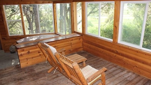 A wooden cabin with a bench, a small table, and large windows offering a view of the outdoors.