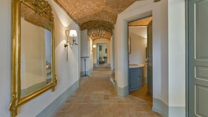 A hallway with a brick ceiling, a large ornate mirror, wall sconces, and a chandelier.