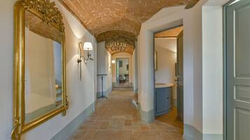 A hallway with a brick ceiling, a large ornate mirror, wall sconces, and a chandelier.