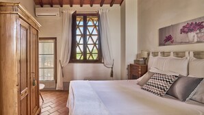 Une chambre à coucher comprenant un lit, une armoire en bois, une fenêtre avec des rideaux, une table de chevet et une lampe fixée au mur.