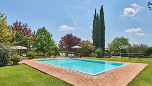 Une piscine rectangulaire bordée de briques, entourée d’une pelouse bien entretenue et de divers arbres.