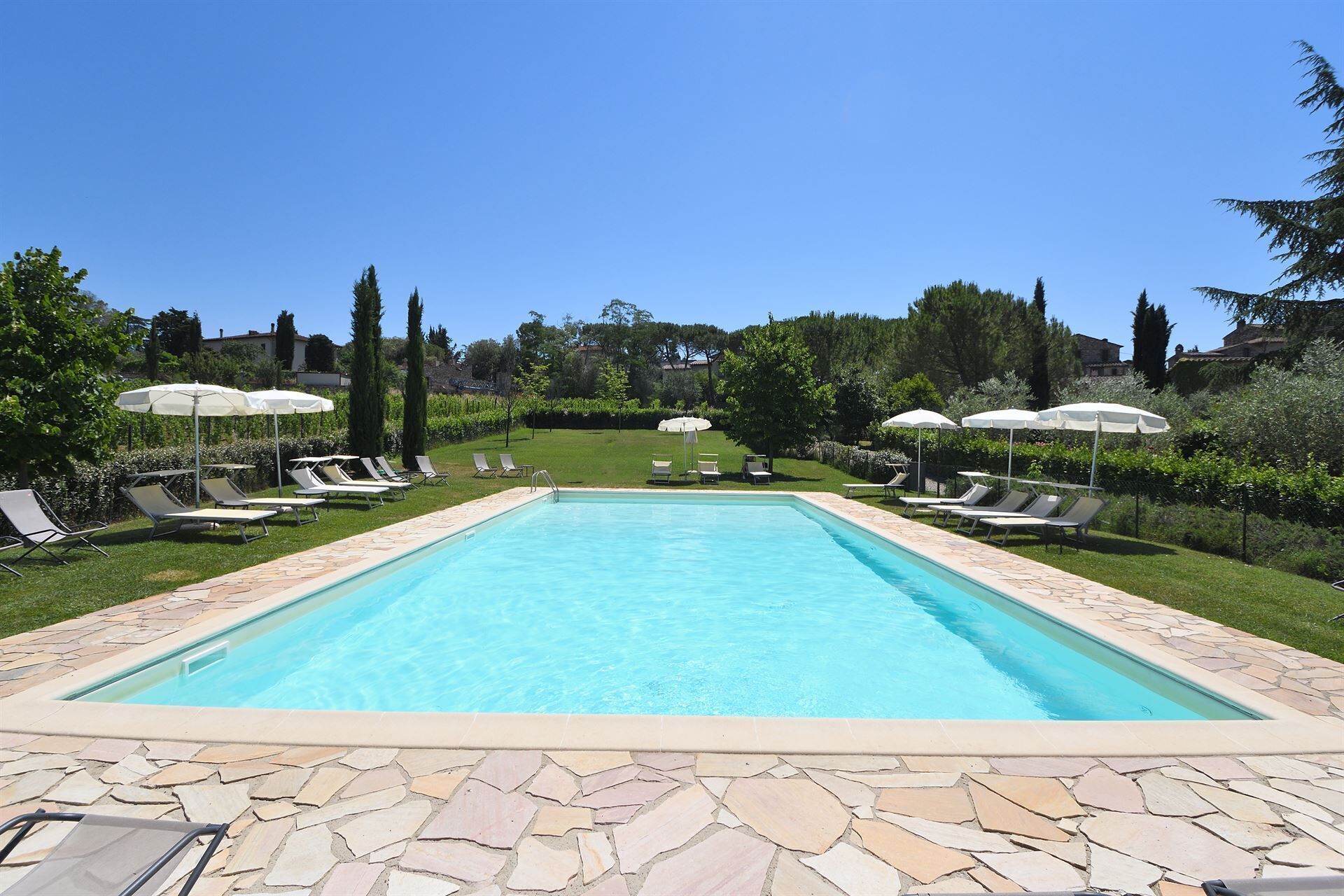 A rectangular swimming pool with a stone border, surrounded by lounge chairs and umbrellas.