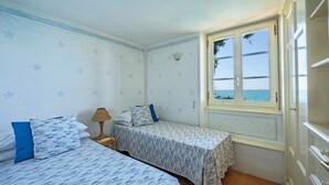 A bedroom with two beds, a window with a view of the sea, and star-patterned wallpaper. - Bellavista, Punta Nera, Monte Argentario, Grosseto and Maremma (Monte Argentario)
