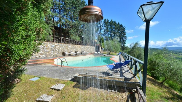 A swimming pool with a stone wall and lounge chairs, surrounded by greenery and a view of the landscape. - Villa Beba, Castellina in Chianti, Siena and Chianti (Castellina in Chianti)