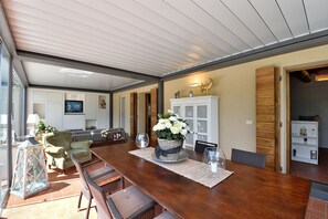 A spacious dining area with a long wooden table, wicker chairs, and a large potted plant.