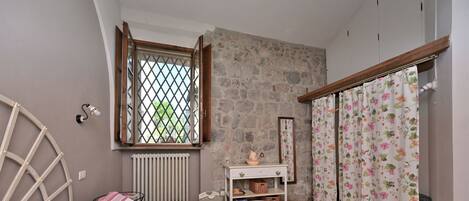 A bedroom with a bed, a radiator, a window with a lattice, a wooden wardrobe, and a floral curtain.