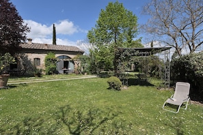 Ein rustikales Steinhaus mit Garten, einer Pergola und einem Metallstuhl.