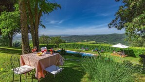 An outdoor dining area with a table set for two, overlooking a pool and lush greenery.