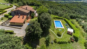 A large house with a swimming pool, surrounded by lush greenery and a scenic view of distant mountains.