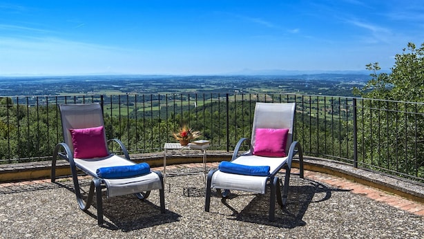 Two lounge chairs with cushions, a small table, and a scenic view of a valley and mountains.