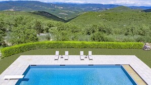 A rectangular swimming pool with a clear blue water surface, surrounded by a paved deck. In the background, there are green hills and a clear sky. - Calafralina, Radda in Chianti, Siena and Chianti (Radda in Chianti)