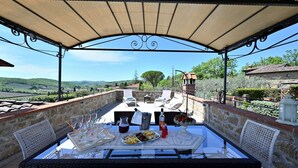 Un área de comedor al aire libre con una mesa preparada para dos, vista al campo y un muro de piedra.