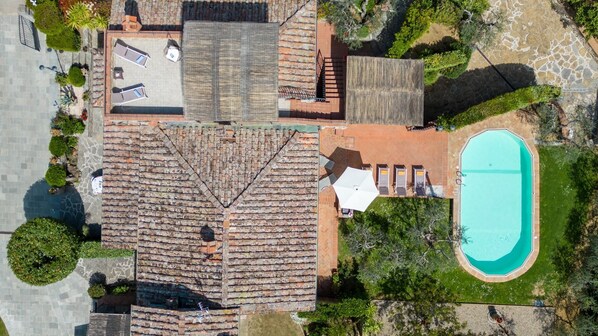 Vista aérea de uma propriedade com piscina, área de varanda coberta e telhado de tijolos.