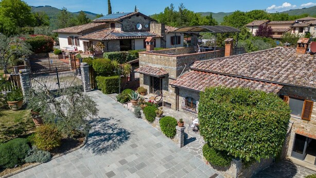 Un patio con edificios de piedra, un área pavimentada y diversas plantas en macetas.