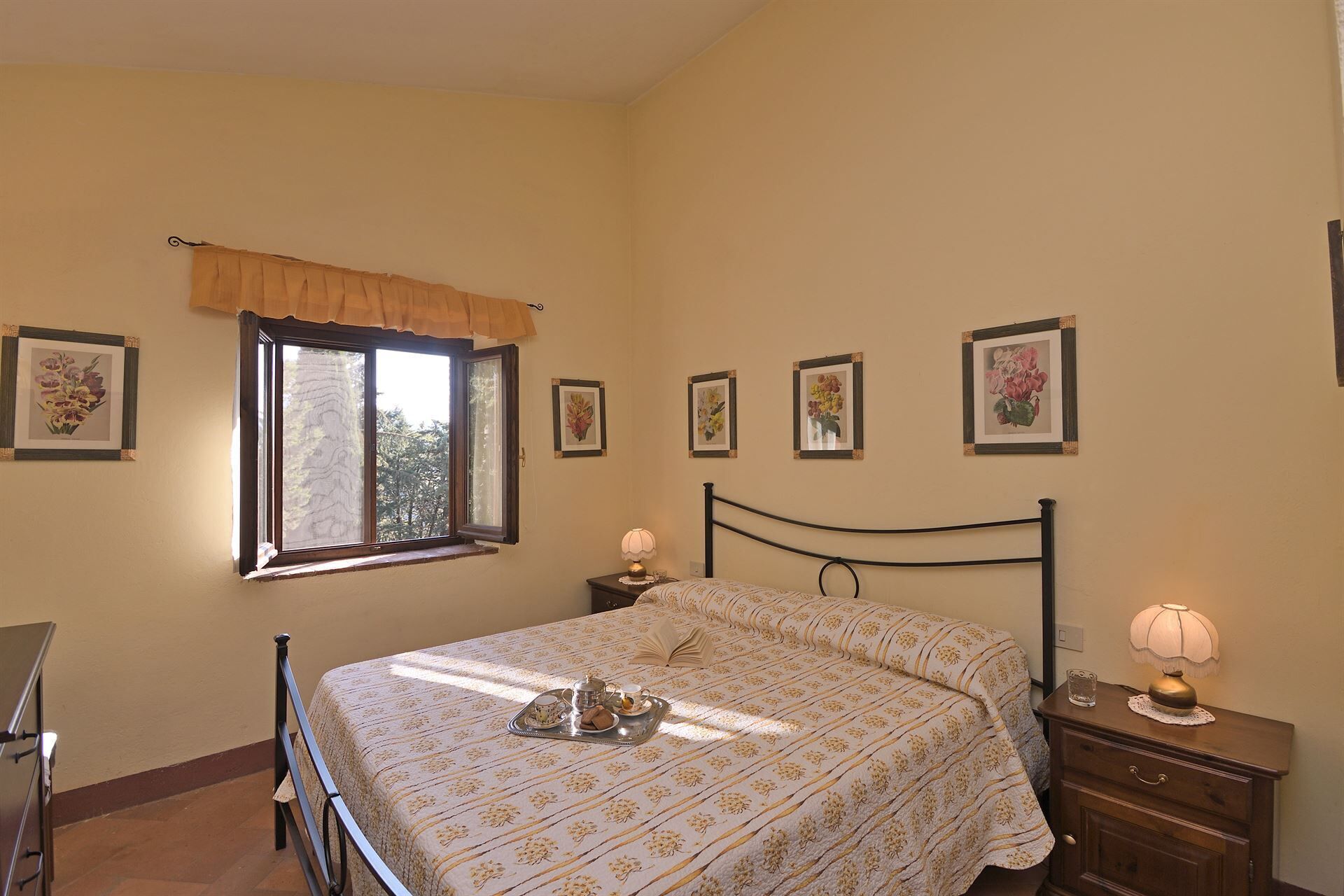 A bedroom with a bed, bedside tables, a window, and floral wall art.