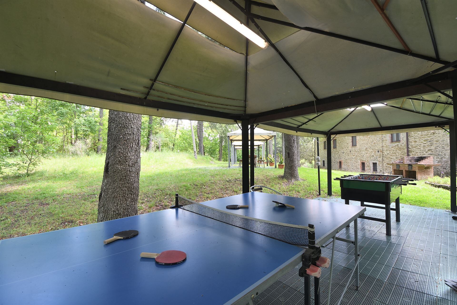 A covered outdoor area with a ping pong table, two paddles, and a foosball table.