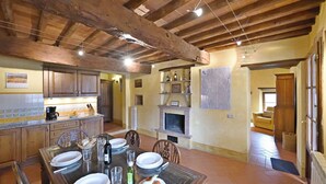 A rustic kitchen with wooden beams, a dining table set for four, and a fireplace. - Pergola, Montebuoni, Gaiole in Chianti, Siena and Chianti (Gaiole in Chianti)